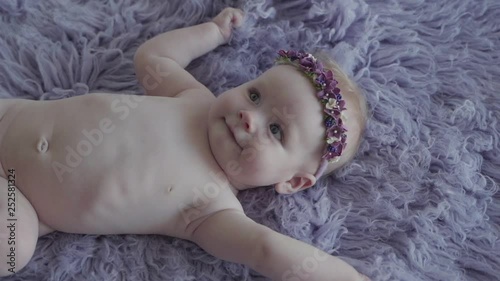 A naked little girl on a photosession on the purple cover smiling in slow motion