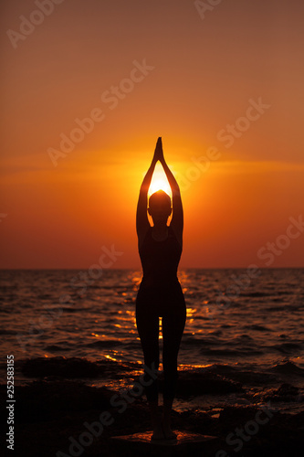 Woman do yoga at sunset by the sea. Silhouette. Meditation and relaxation.