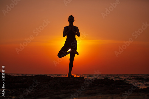 Woman do yoga at sunset by the sea. Silhouette. Meditation and relaxation.