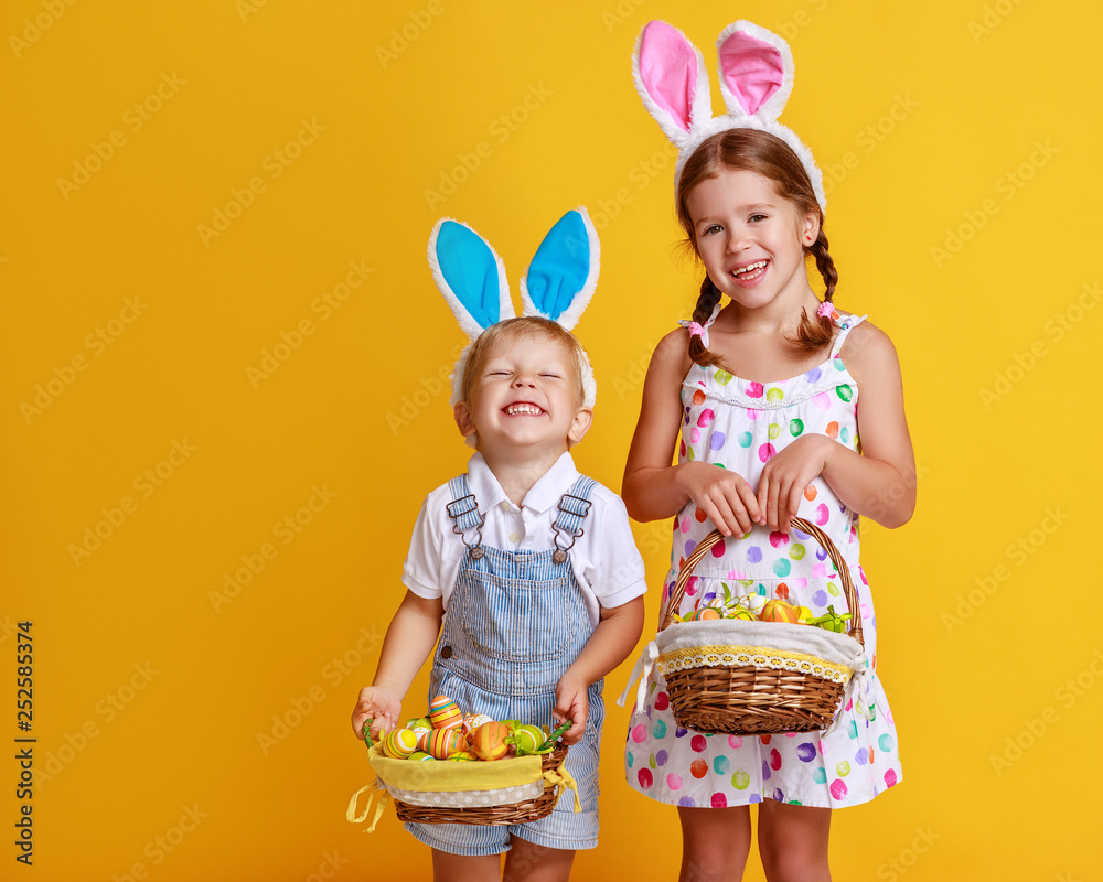 funny happy child boy with easter eggs and bunny ears on yellow.