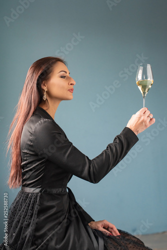 Modern sommelier estimating smell of wine in wineglass. Attractive joyful female model in a black dress with wine glass in hand with pleasure. Adorable caucasian girl at festive and tasting red wine.