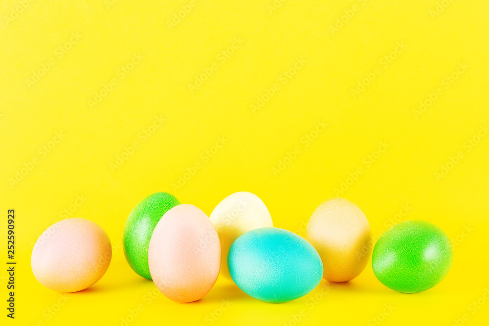 Bunch of blank painted Easter eggs of different pastel color isolated on bright yellow background with a lot of copy space for text. Front view, flat lay, close up.