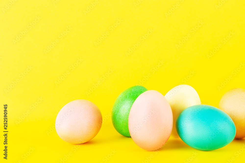 Bunch of blank painted Easter eggs of different pastel color isolated on bright yellow background with a lot of copy space for text. Front view, flat lay, close up.