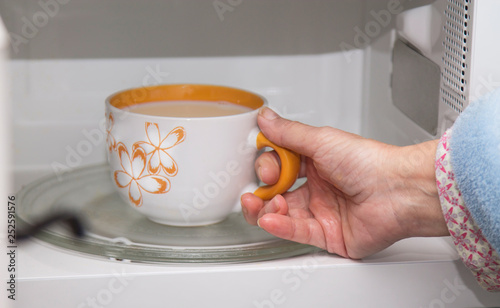 woman hand using are bringing coffe cup to the microwave oven at home. To reheat frozen food for their. Cooking made easy concept.