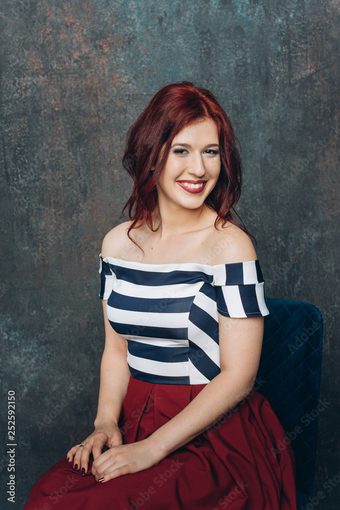 Naklejka premium Attractive bright redhaired smiling woman in striped blouse on green background
