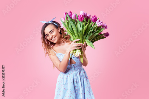 Young happy smiling redhead woman holding bouquet of colorful spring flowers isolated on pink background. Pink tulips, festive bouquet in honor of women's day on March 8 or birthday