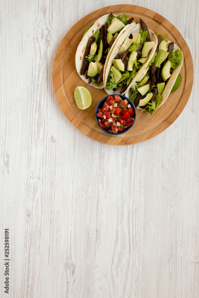 Corn tortillas with grilled beef, avocado, lime and salsa on bamboo board, overhead view. From above, top view. Copy space. Corn tortillas with grilled beef, avocado, lime and salsa on bamboo board, overhead view. From above, top view. Copy space.