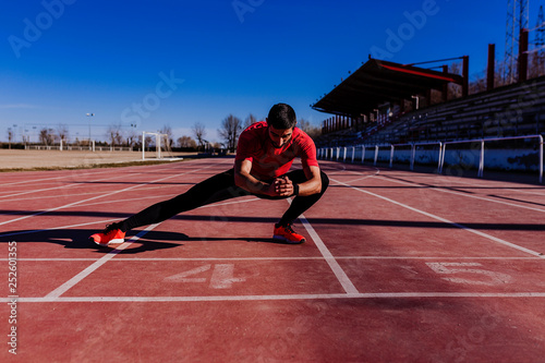 young muscular athlete is at the start of the race tracks line at the stadium. Sports concept