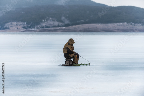 Ice fisherman on frozen winter mountain lake