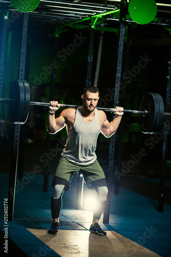 Man with heavyweight barbell in the dark gym.