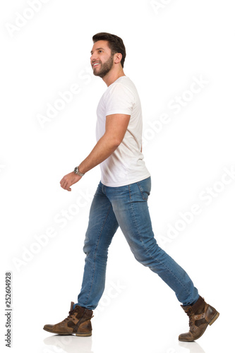 Young Man In Jeans And White T-shirt Is Walking And Looking Away. Side View.