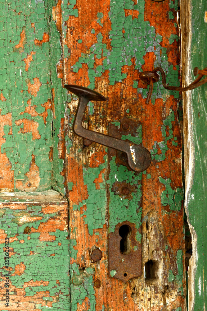 Rusty doorknob and latch on old weathered green door .
