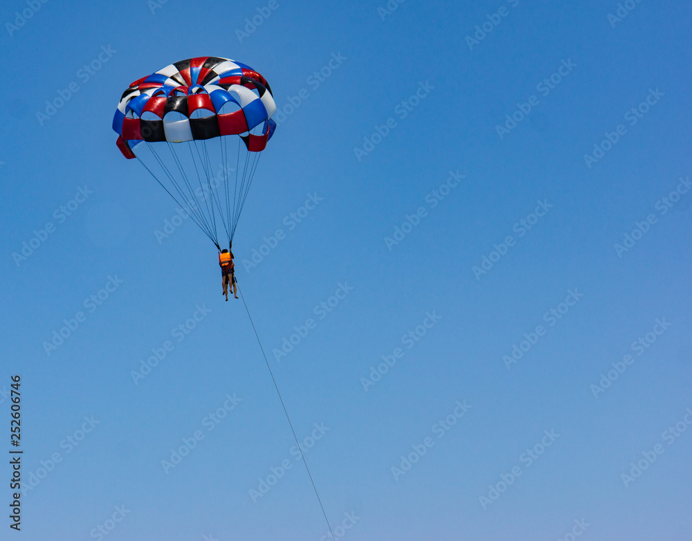 parasail with two swimmers hanging above the ocean while being pulled by motor boat parasail with two swimmers hanging above the ocean while being pulled by motor boat
