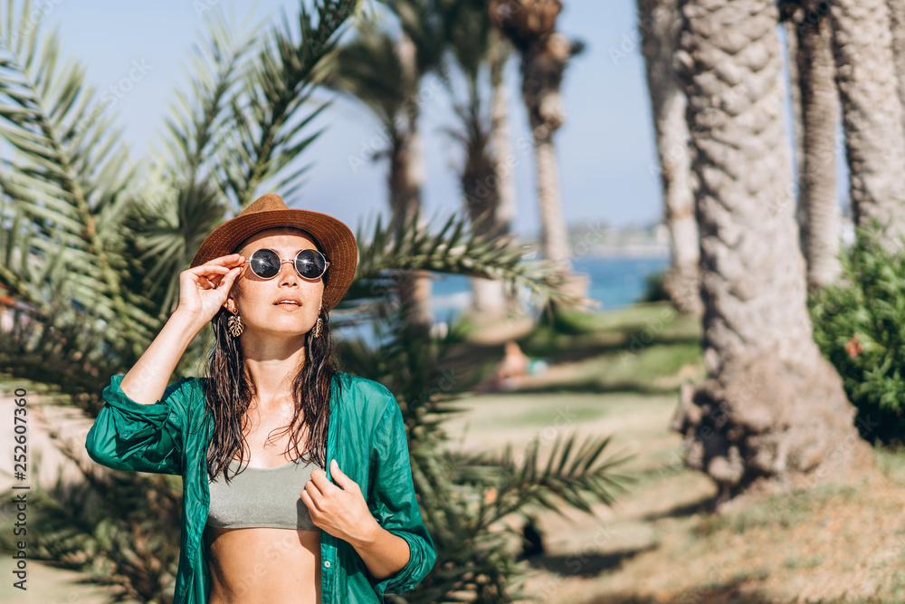 Cute pan asian girl in hat and sunglasses in green pareo walking on the seaside. Cute pan asian girl in hat and sunglasses in green pareo walking on the seaside.