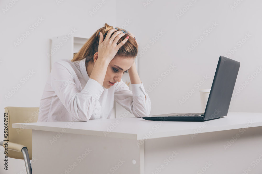 Young attractive woman at modern office desk, working on laptop, massaging temples to forget about constant headaches, noisy loud office giving a migraine, relieving stress, chronic pain Young attractive woman at modern office desk, working on laptop, massaging temples to forget about constant headaches, noisy loud office giving a migraine, relieving stress, chronic pain