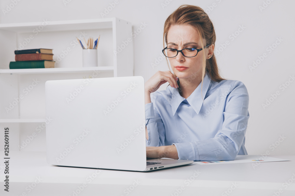 Serious woman in the glasses working her laptop. Office woman looks tired