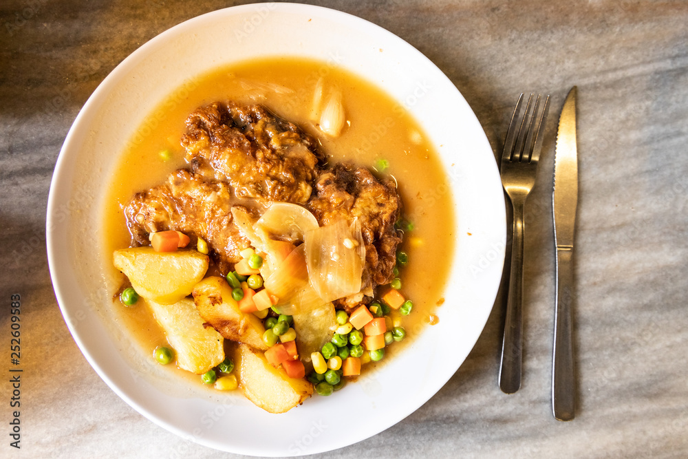 Serving of hainanese chicken chop with gravy, peas, carrots, potatoes.