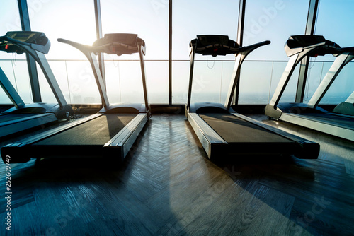 treadmills row in fitness gym with window and sunset background
