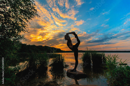 Blonde woman doing bow pulling pose outdoors on a stone in the lake. Yoga nature concept. photo