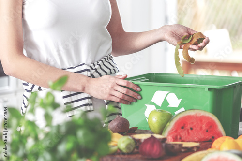 Closeup of eco friendly woman in the kitchen disposing of leftovers of kiwi into compost bin while preparing fruit salad