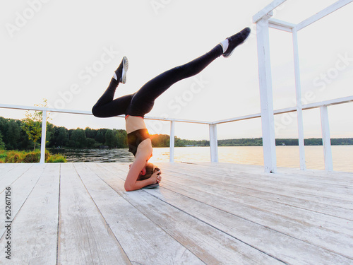 Blonde woman doing headstand on a white wooden lake pier. Yoga nature concept.