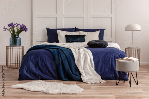 Purple flowers in glass vase and lamp on stylish nightstands on both sides of cozy bed
