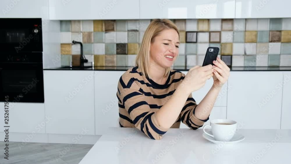 Cute young girl student communicates with her mom in social networks using a smartphone while sitting at a table with a cup of hot coffee in her cozy designer kitchen Cute young girl student communicates with her mom in social networks using a smartphone while sitting at a table with a cup of hot coffee in her cozy designer kitchen