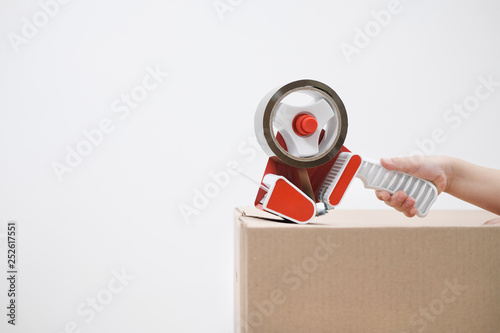 The hand of the child seals the cardboard boxes with a dispenser and adhesive tape. photo