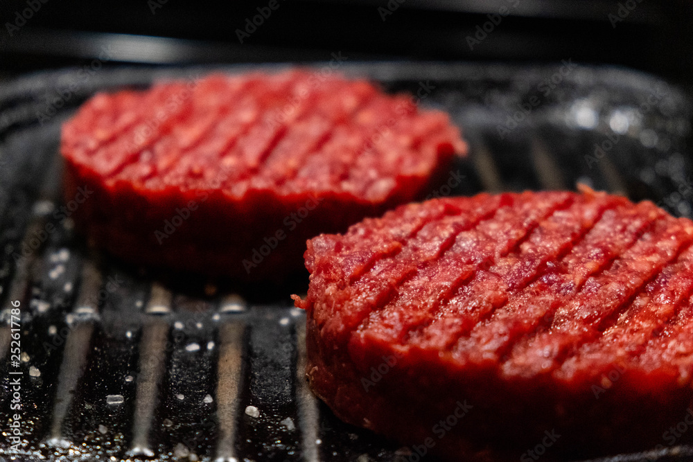 Raw grilled hamburgers with onions closeup. Dark background.