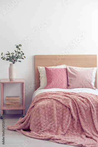 Pink pillows and cozy blanket on single bed in elegant hotel room, copy space on empty white wall © Photographee.eu