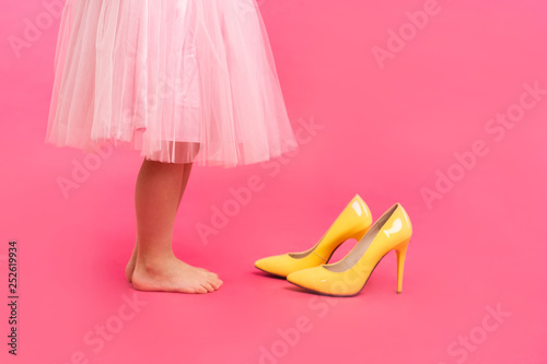 Little girl in oversized shoes with space for text, closeup on legs isolated on pink.