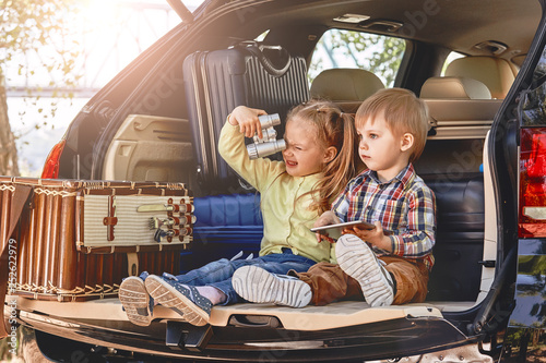 Little cute kids having fun in the trunk of a car with suitcases. Family road trip