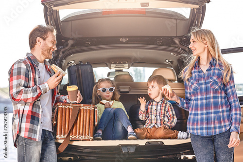 Snack time. Family stands near the car, having a lunch. Family road trip photo