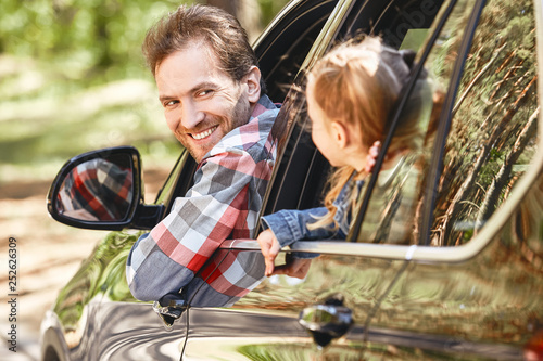 To travel is to live. Father and daughter looking out the car window and smiling happily to each other. Family road trip photo