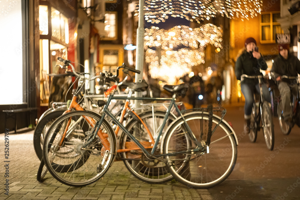 young hipsters cyclists ride past bicycle parking in a European city late at night. bokeh and blur