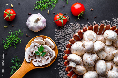 Fresh sliced champignon in wooden spoon on a black background. Cooking homemade dishes of white ripe mushroom with parsley, dill and vegetables.