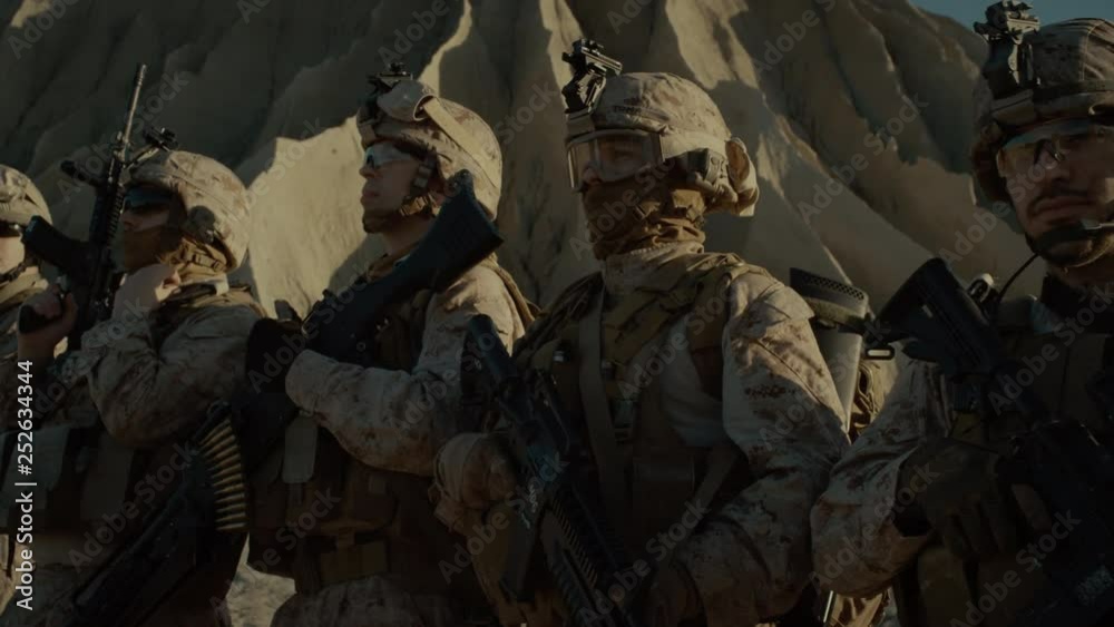 Close-up Moving Shot Group of Fully Equipped Soldiers Standing in a Line in the Desert. Paratroopers Ready for the Mission in Desert Region Close-up Moving Shot Group of Fully Equipped Soldiers Standing in a Line in the Desert. Paratroopers Ready for the Mission in Desert Region