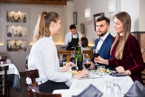 Group of smiling friends enjoying evening meal at restaurant