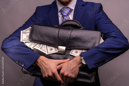 A man holding in his hands a full bag of money in dollars, which from it drop out. Concept on the topic of corruption and impunity of financial crimes in USA.