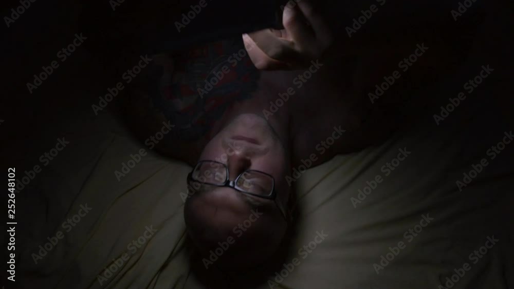 Middle-aged adult male using mobile phone, smartphone on bed at night, texting and flipping social networks Middle-aged adult male using mobile phone, smartphone on bed at night, texting and flipping social networks