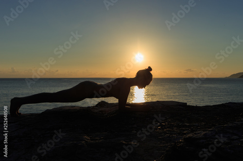 Young female silhouette doing plank exercise on a beach at sunrise photo