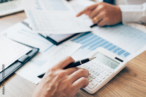 Manager calculates about the company finances by pressing on the calculator on the table with the employee explaining the summary report of the company cost at the office.