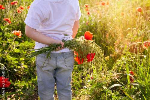 Child boy with a bouquet of flowers. In the flower field, wild poppies.