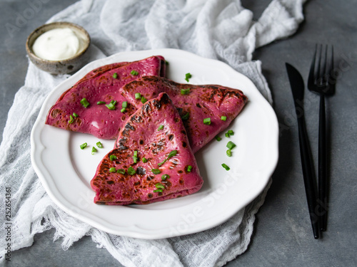 Red beetroot pancakes, pink thin beet crepes stuffed with cream cheese and green onions on gray background. Shrovetide Maslenitsa Butter Week festival meal. Close up, selective focus. Breakfast
