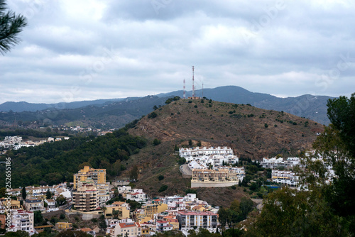 View of the mountains and the Spanish city of Malaga from the observation deck of the fortress of Gibralfaro. Spain, Andolusia, Costa de Sol. Sky, mountains and buildings on a cloudy day.