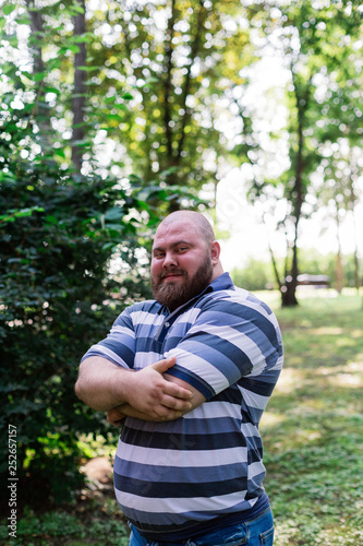 Fat man in the park looks into the frame, a portrait of a man with excess weight.