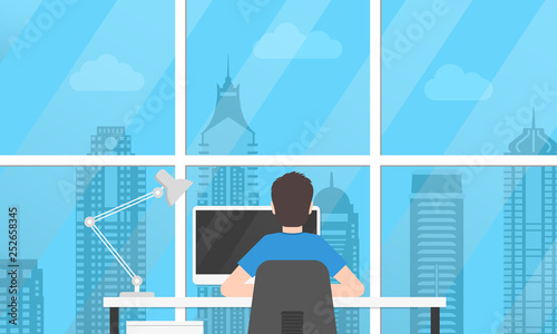 Man is working on the computer in the modern office near the window with skyscrapers view. Person sitting on a chair in the office desk or table. Back view. Business workplace or workspace concept.