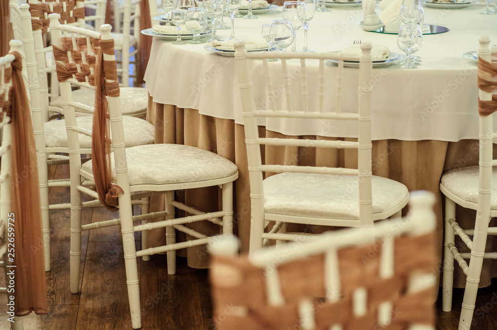 close up photo of white chairs decorated with brown textil in a banquet hall in white and brown colors decorated for the event