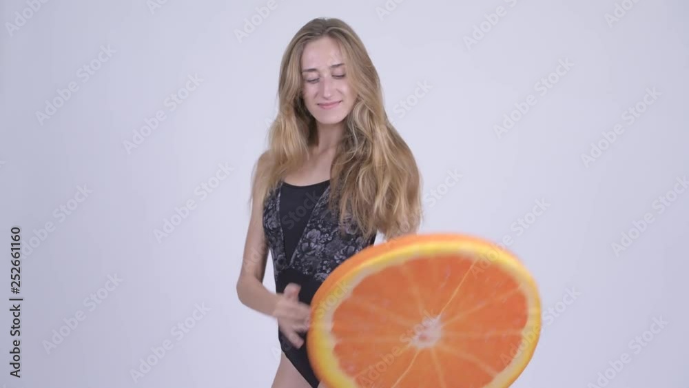 Happy young blonde woman in swimsuit biting orange pillow as healthy concept Happy young blonde woman in swimsuit biting orange pillow as healthy concept
