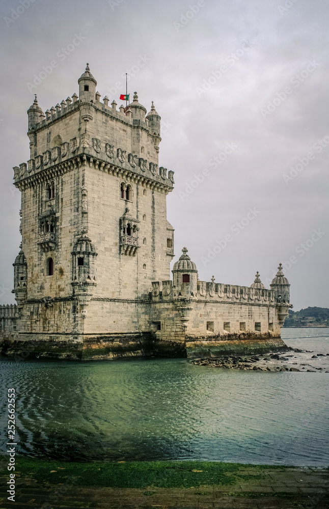 Torre de Belém in Lisbon as seen on a moody day with grey sky and green blue water (Lisbon, Portugal, Europe)
